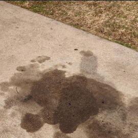 A close-up view of concrete pavement covered with dark, wet oil stains and deep discoloration.