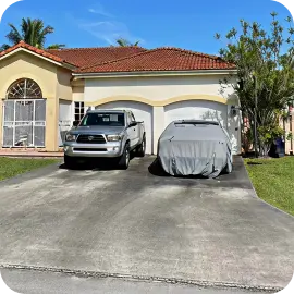 A stained concrete driveway leading to a two-car garage with a silver pickup truck and a covered car parked outside.