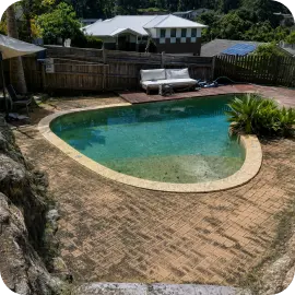 An uncleaned brick paver pool deck covered with dark grime and weathered stains surrounding an outdoor swimming pool.