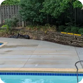 A concrete pool deck next to blue pool tile showing uneven, faded, and cloudy patches where the existing sealer is failing.