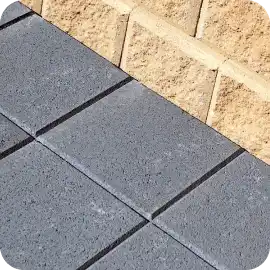 A close-up view of newly installed dark gray textured stone pavers bordered by a tan concrete block retaining wall.